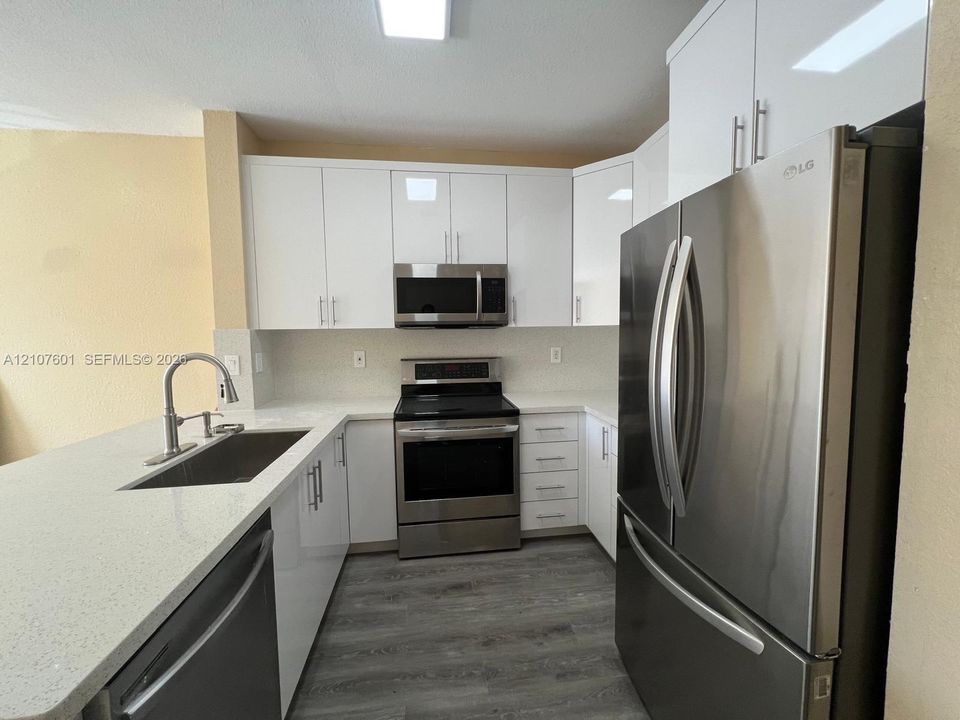 Kitchen featuring high-gloss white cabinetry, white stone countertops, stainless steel appliances, a stainless steel undermount sink with a gooseneck faucet, and grey wood-finish flooring