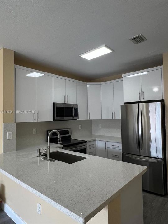 Kitchen featuring white flat-panel cabinetry, quartz countertops, a stainless steel undermount sink with a gooseneck faucet, and stainless steel appliances