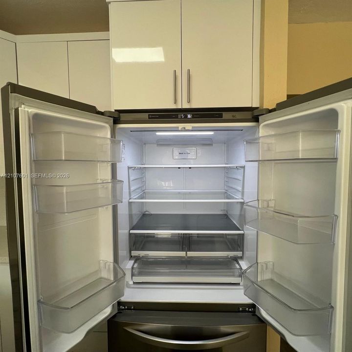 Stainless steel French-door refrigerator featuring adjustable glass shelving and high-gloss white cabinetry
