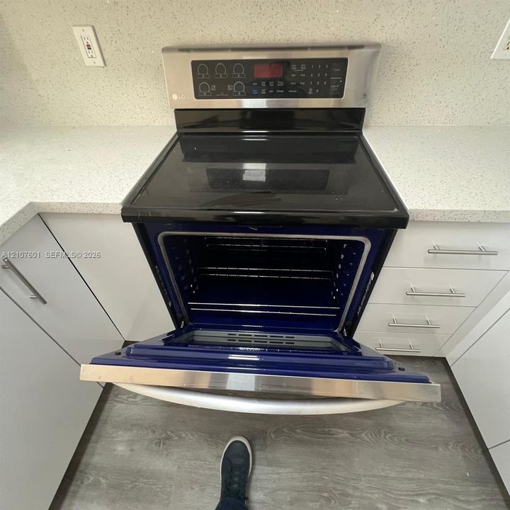 Stainless steel slide-in electric range featuring a black glass cooktop, solid-surface countertops, white flat-panel cabinetry with brushed nickel hardware, and wood-finish flooring