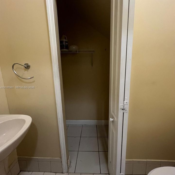 Wall-mounted chrome towel ring, pedestal sink with ceramic basin, and tiled flooring