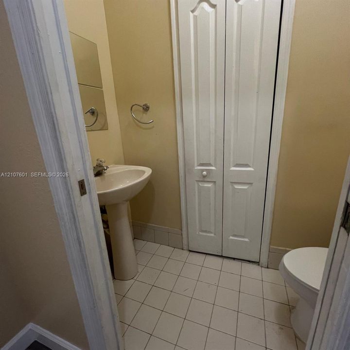 Pedestal sink with polished metal faucet, tiled flooring, wall-mounted towel ring, and bi-fold door closet