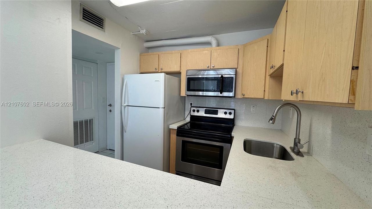 Kitchen featuring light-finish cabinetry, solid surface countertops, stainless steel appliances, and a stainless steel gooseneck faucet