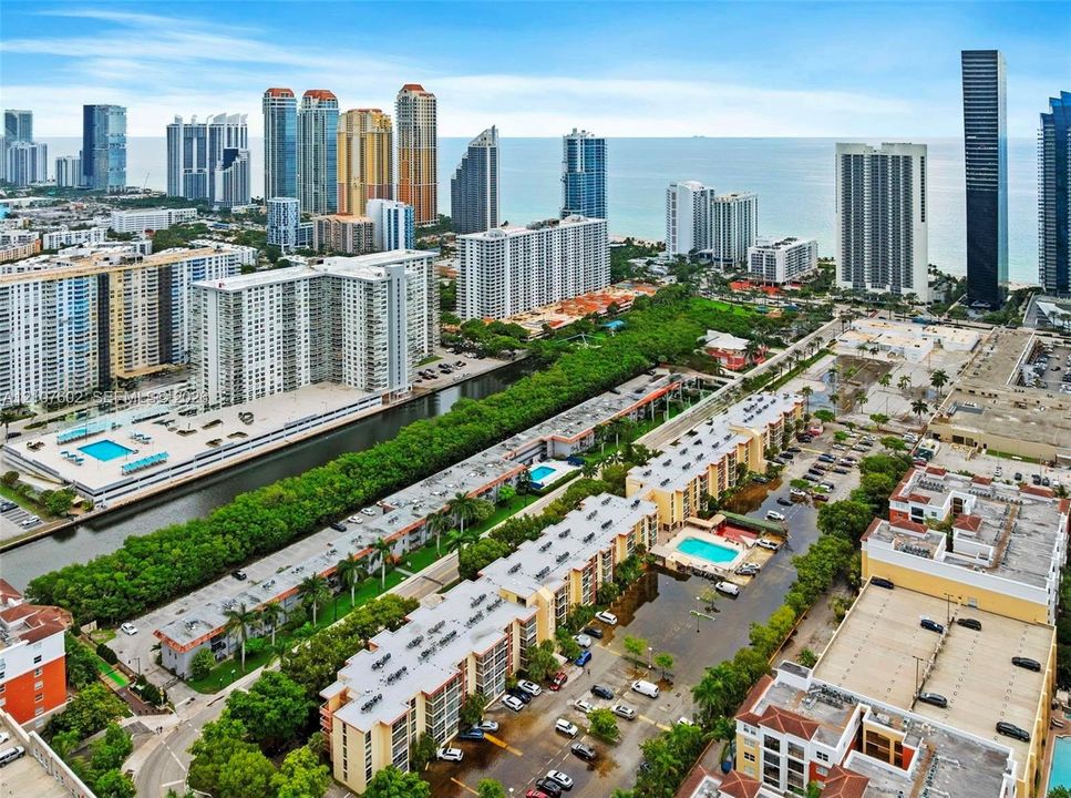 Aerial perspective featuring multiple mid-rise residential structures, surface parking areas, landscaped grounds, and proximity to an urban coastline