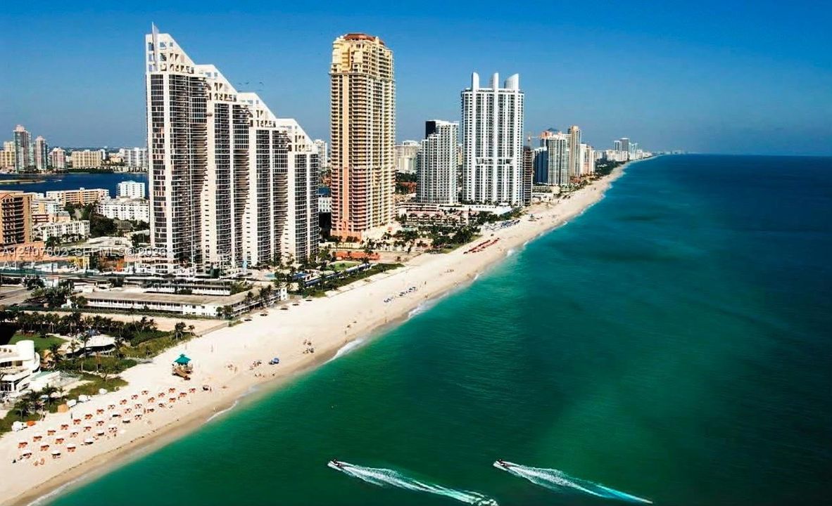 Aerial perspective of coastal high-rise development featuring direct oceanfront access, sandy shoreline, and expansive water frontage