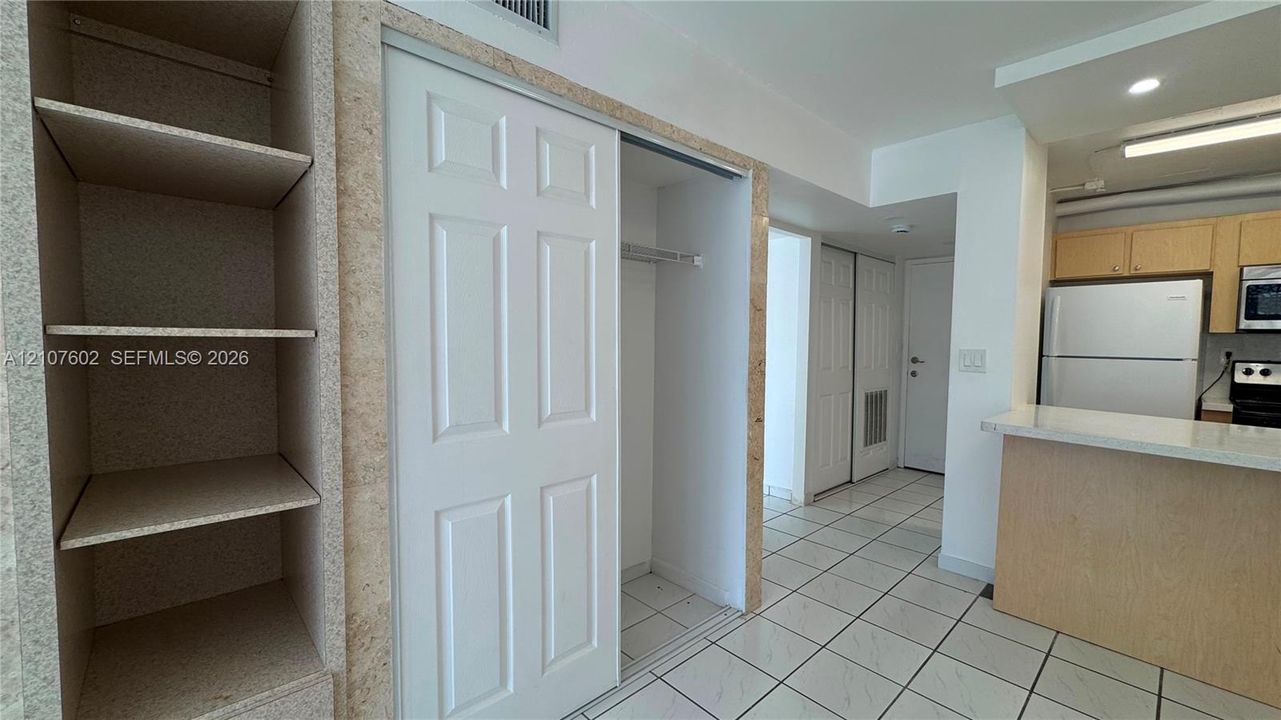Built-in shelving, white sliding-door closet, tiled flooring, and breakfast bar with stone-surfaced countertop