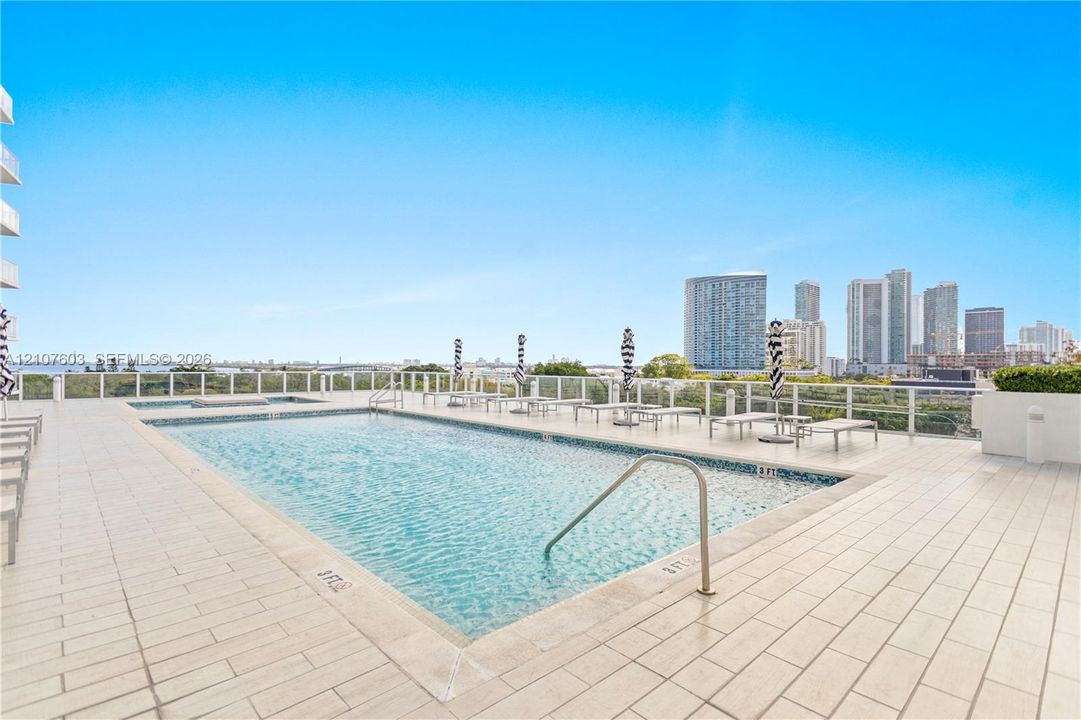 Rooftop swimming pool with tile decking, metal handrails, and glass panel perimeter fencing