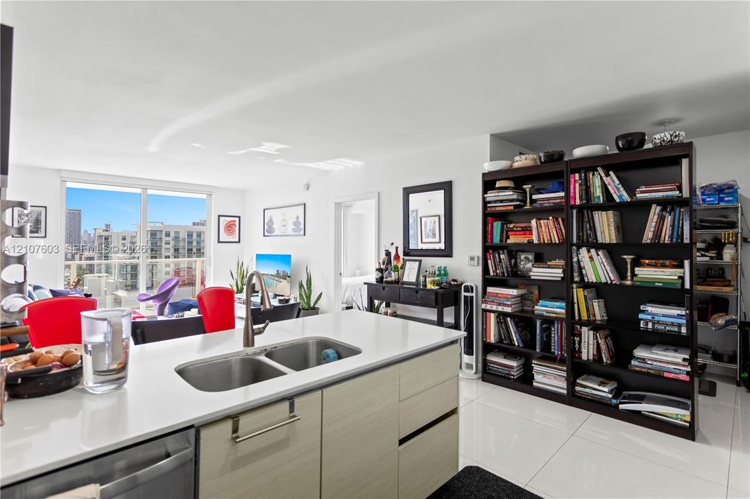 Kitchen island featuring a white countertop, stainless steel dual-basin sink, and light-tone cabinetry with horizontal grain, complemented by white polished floor tiling and floor-to-ceiling glass sliding doors