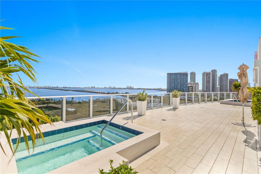 Expansive outdoor terrace featuring light-toned tile flooring, an in-ground spa with tile surround, and a glass-paneled railing