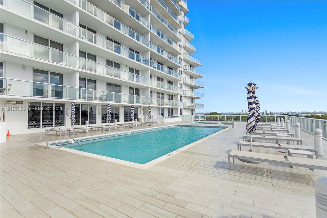 In-ground swimming pool with tile border, sprawling ceramic tile pool deck, and multi-story high-rise building featuring private glass-paneled balconies
