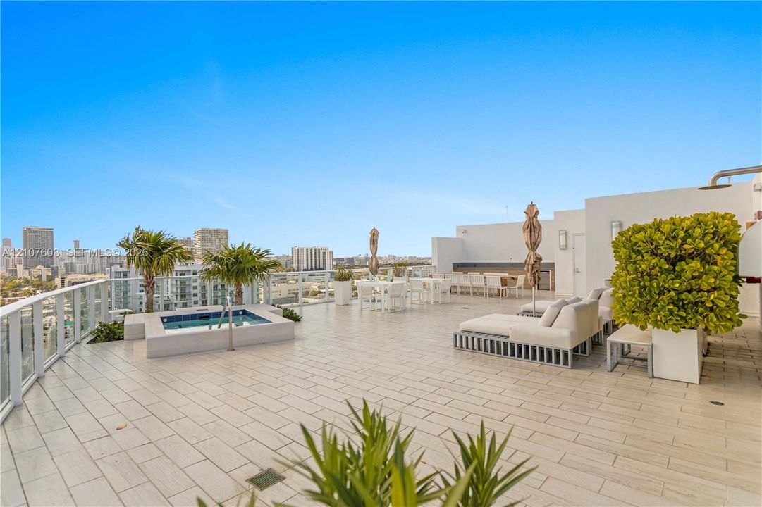 Expansive rooftop terrace featuring large-format tile flooring, a built-in spa, glass railing, and integrated exterior wall lighting