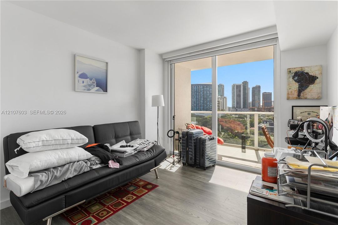 Floor-to-ceiling sliding glass door, private balcony with metal railing, and wood-finish flooring