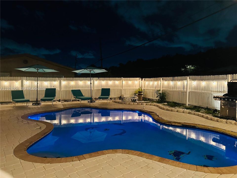 Freeform swimming pool with stone coping, paver patio, and privacy fencing