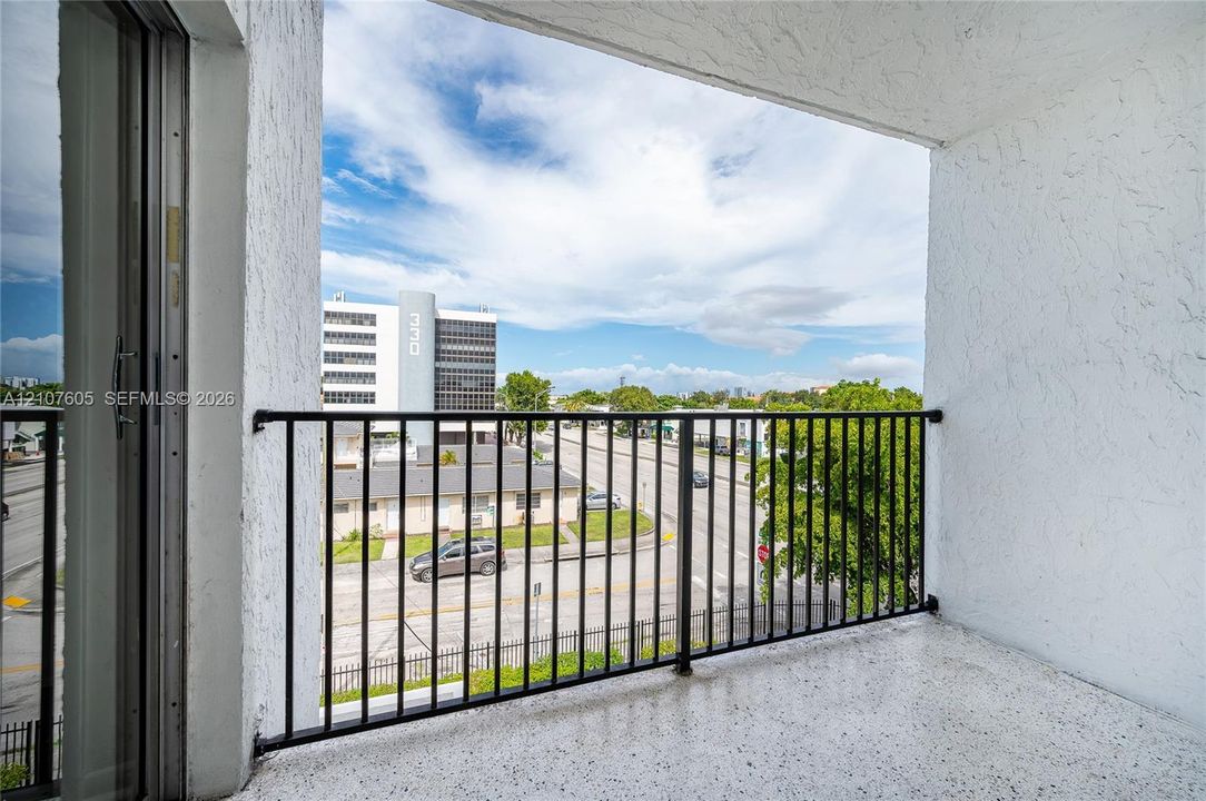 Covered balcony featuring textured concrete walls, speckled flooring, and a black metal railing