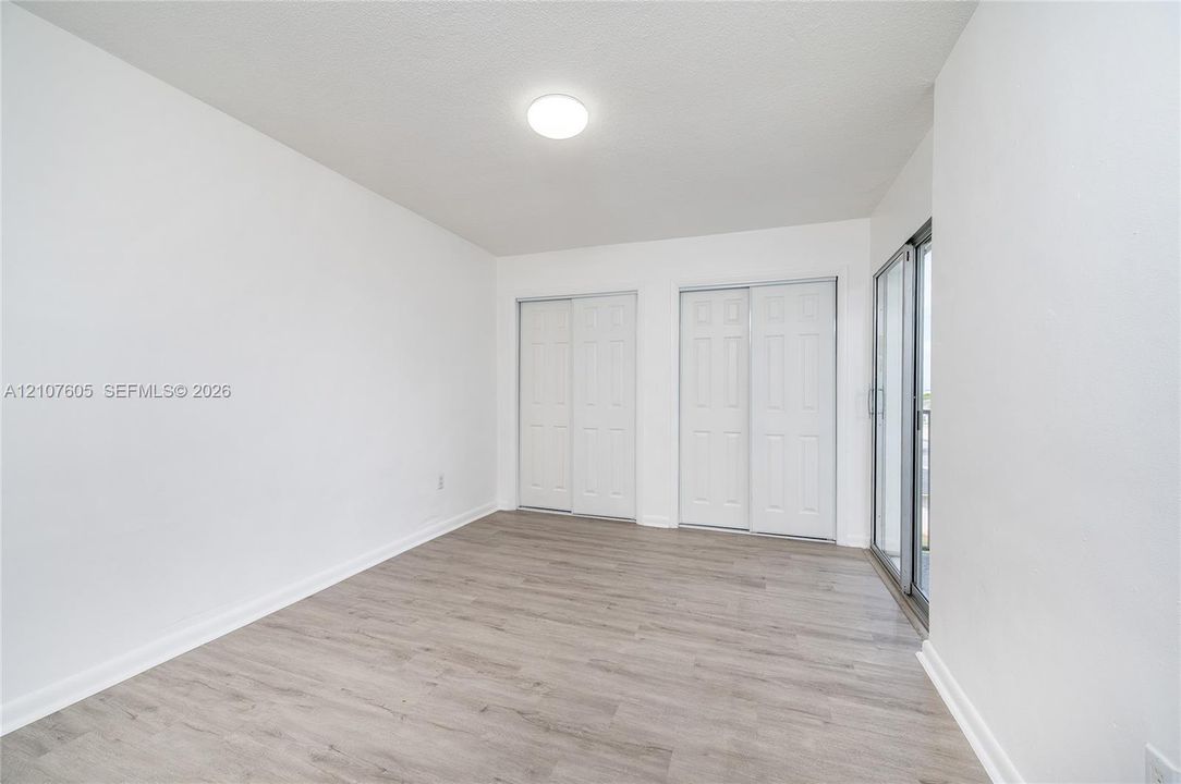 Room featuring wood-finish flooring, two sets of white double-door closets, and a glass sliding door