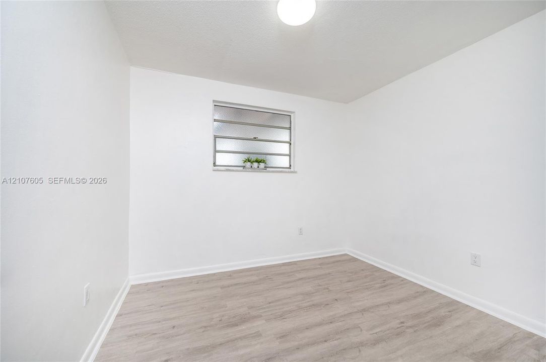 Neutral interior space featuring wood-finish flooring, crisp white walls, a flush-mount ceiling light, and jalousie-style window