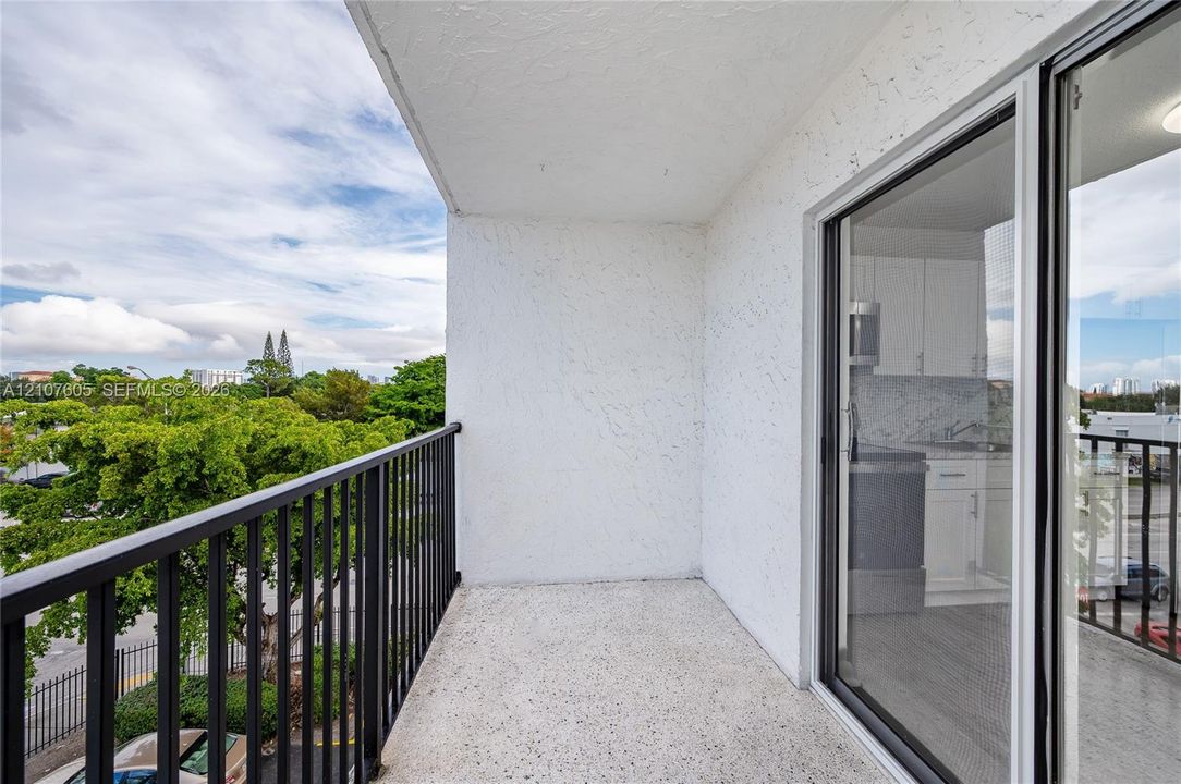 Private balcony featuring a concrete floor, black metal railing, and textured stucco walls, accessible via sliding glass doors