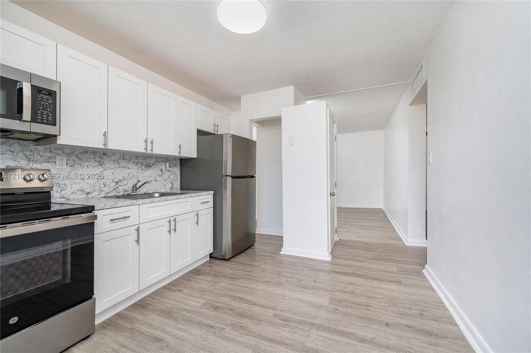 Kitchen featuring white Shaker-style cabinetry, stainless steel appliances, stone-patterned backsplash, and wood-finish flooring