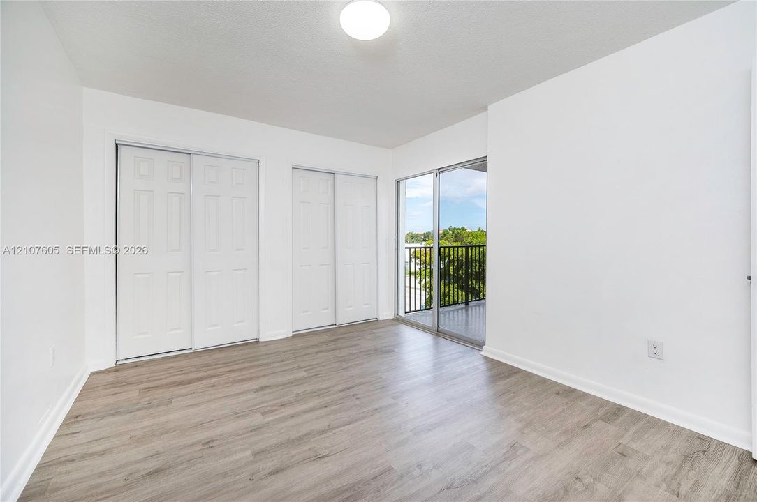 Room featuring wood-finish flooring, dual sliding-door closets with paneled detailing, and a glass sliding door providing access to an exterior balcony