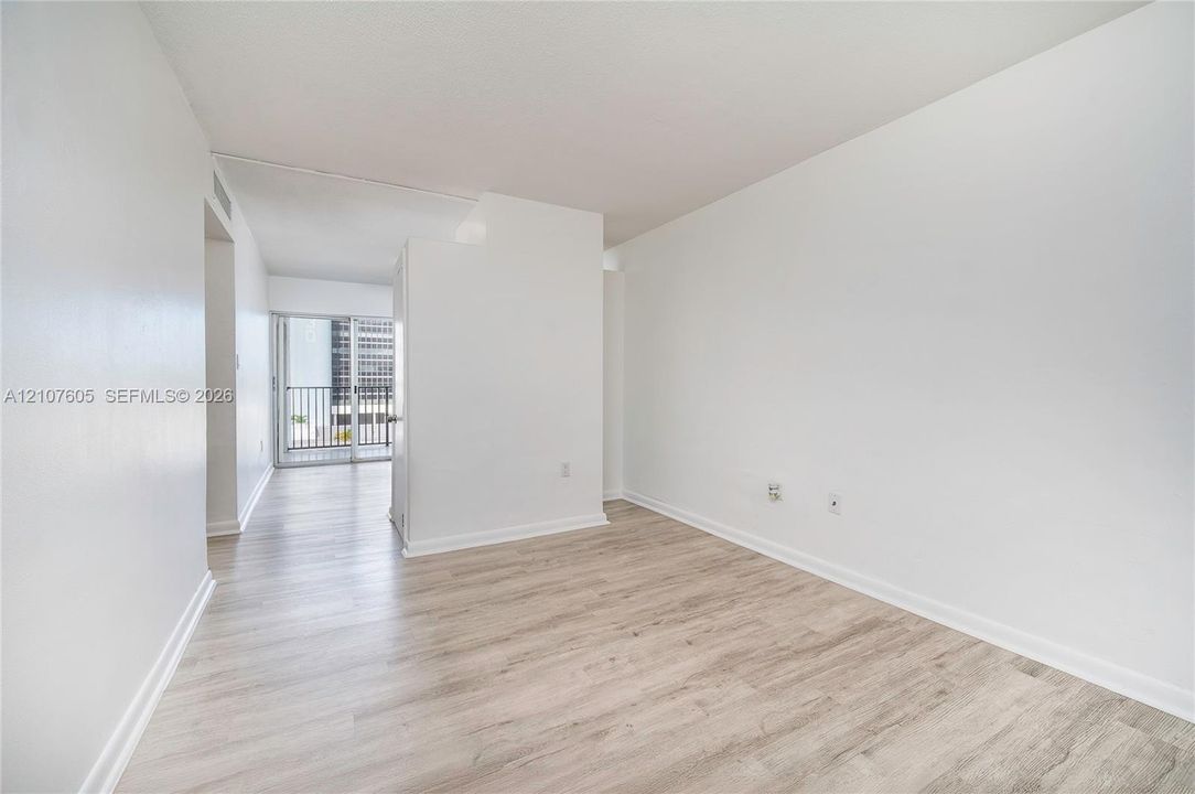Neutral interior space featuring wood-finish flooring, smooth white walls, and sliding glass doors with access to a railed balcony