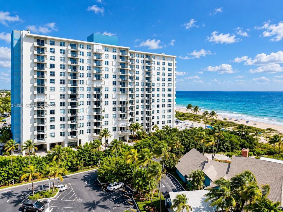 High-rise residential building featuring private balconies, asphalt parking area, and direct proximity to the oceanfront