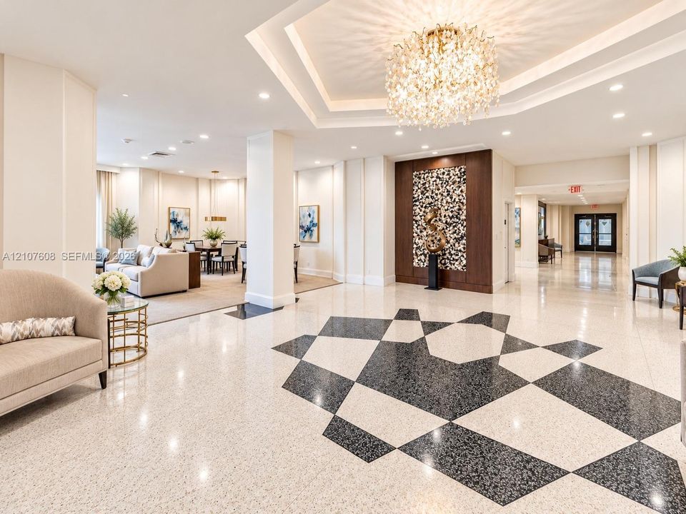 Grand lobby featuring geometric patterned terrazzo flooring, a coffered tray ceiling, a central crystal chandelier, and a decorative wood-paneled accent wall
