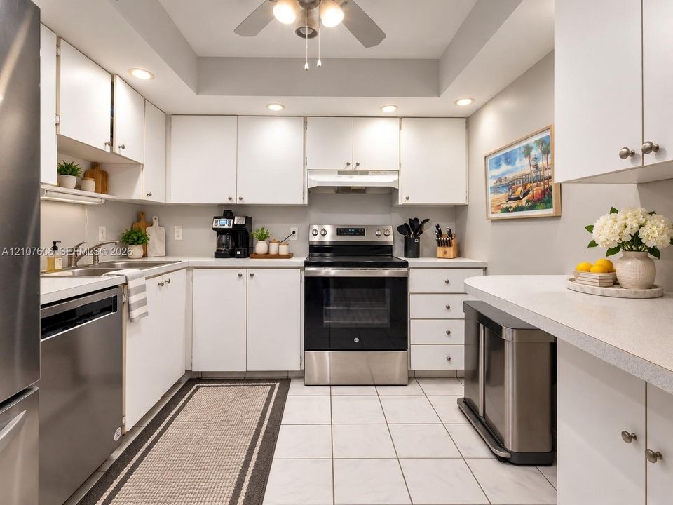 Kitchen featuring white shaker-style cabinetry, stainless steel appliances, recessed ceiling lighting, light-toned tiled flooring, and a peninsula countertop