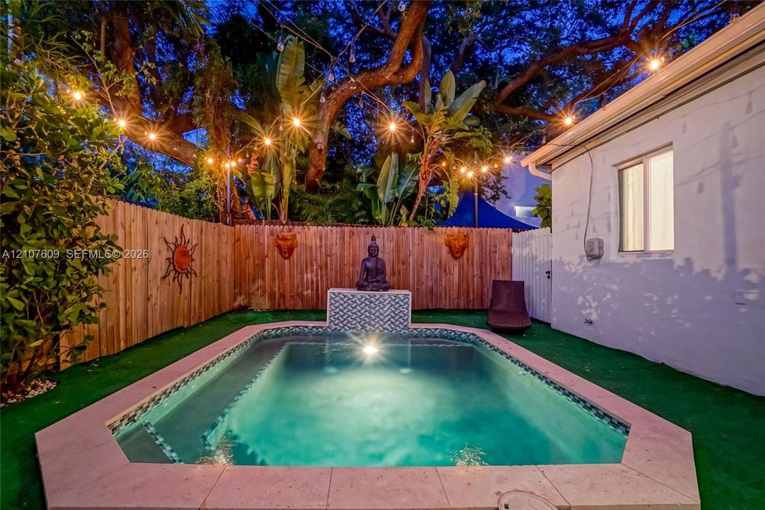 Private rear grounds featuring a custom swimming pool with patterned tile water feature, perimeter wood privacy fencing, and mature tropical landscaping
