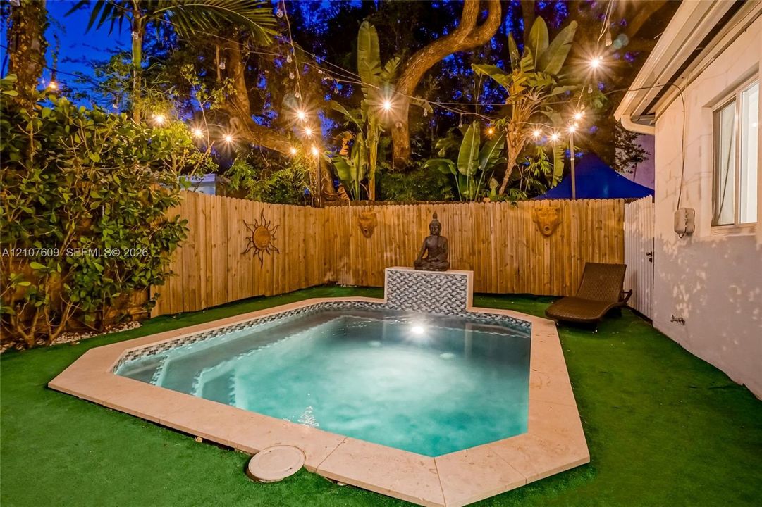 In-ground pool featuring a stone-paver coping, tile-accented water feature, and integrated steps, enclosed by a wood privacy fence