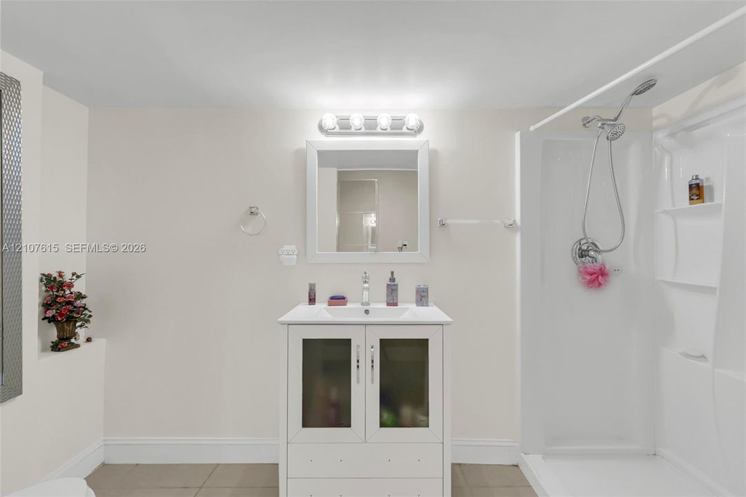 Bathroom featuring a white vanity with frosted glass cabinet doors, a rectangular undermount sink, a framed wall mirror, polished chrome hardware, and a walk-in shower enclosure