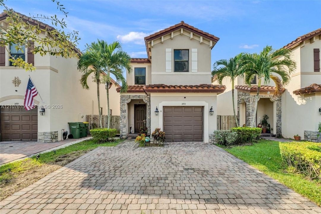 Two-story stucco exterior featuring stone veneer accents, a tiled roof, and a paved brick driveway