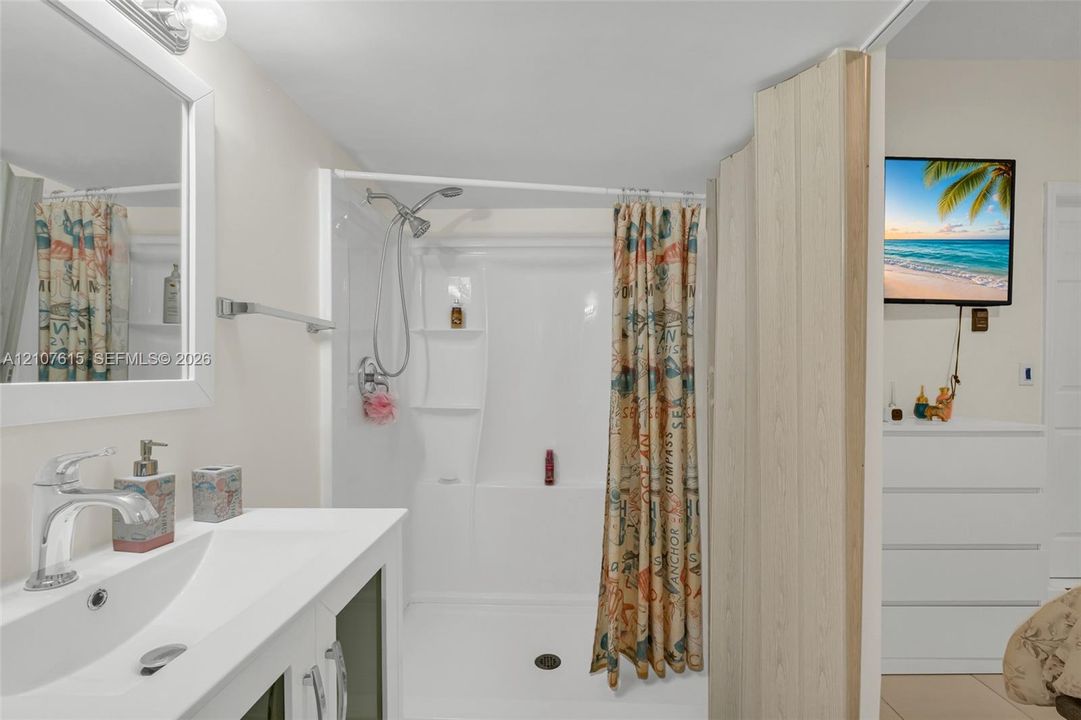 Bathroom featuring a white vanity with an integrated sink, a chrome single-handle faucet, a wall-mounted mirror with a white frame, and a shower enclosure with built-in shelving and a handheld showerhead