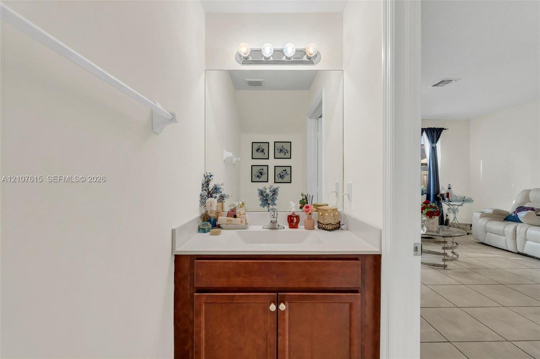 Vanity featuring a wood-finish cabinet, stone-composite countertop with an integrated sink, polished metal faucet, and a wall-mounted light fixture above a large mirror