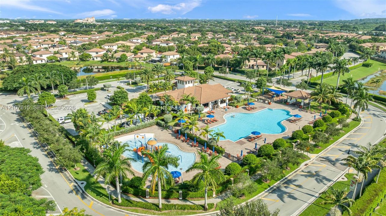 Community recreation area featuring a large swimming pool, shallow splash pool with water features, covered pavilion, and surrounding palm landscaping