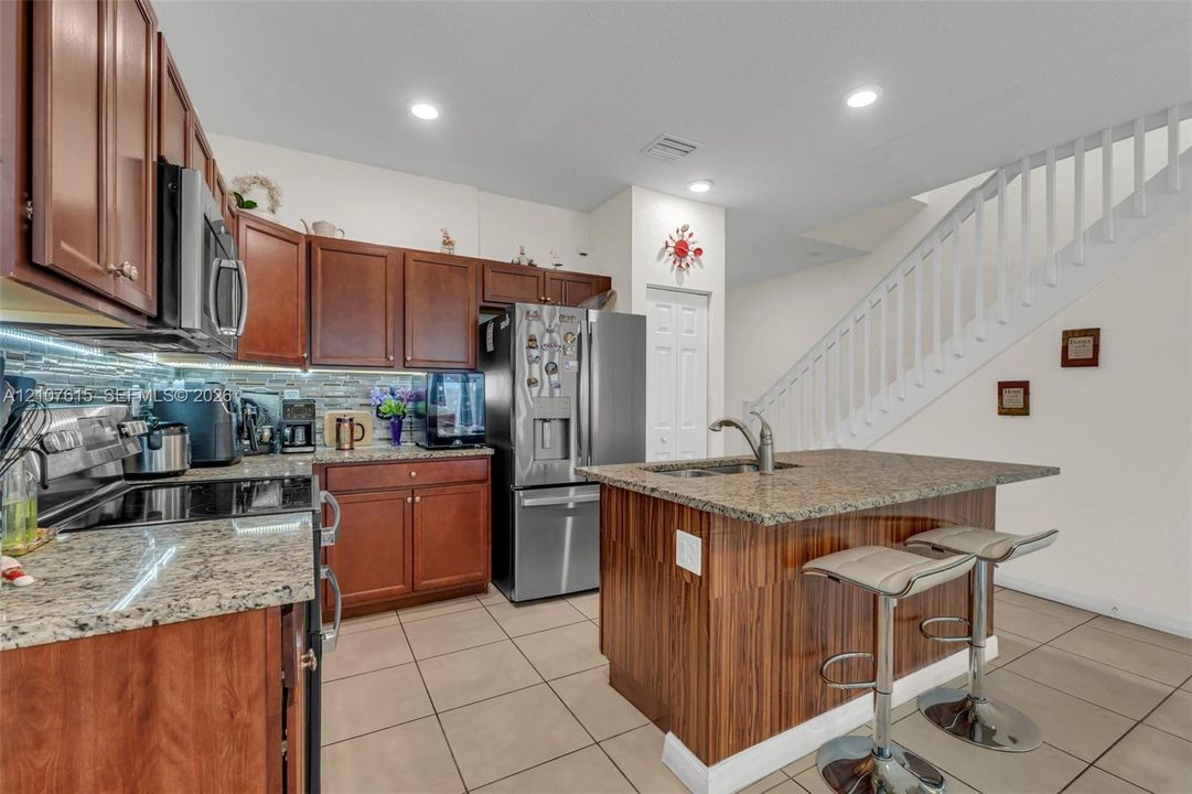 Kitchen featuring stained wood cabinetry, stone countertops, stainless steel appliances, a center island, and tile flooring