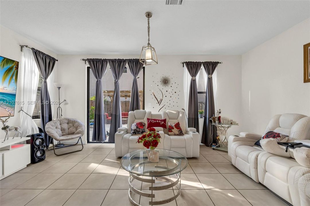 Living area featuring neutral tile flooring, recessed ceiling lighting, a contemporary metal pendant fixture, and sliding glass doors