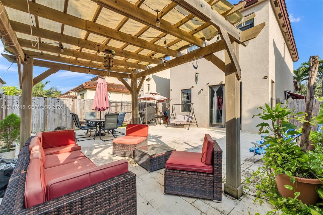 Backyard patio featuring a wood-beam pergola, light-toned stone paver flooring, and perimeter wood fencing