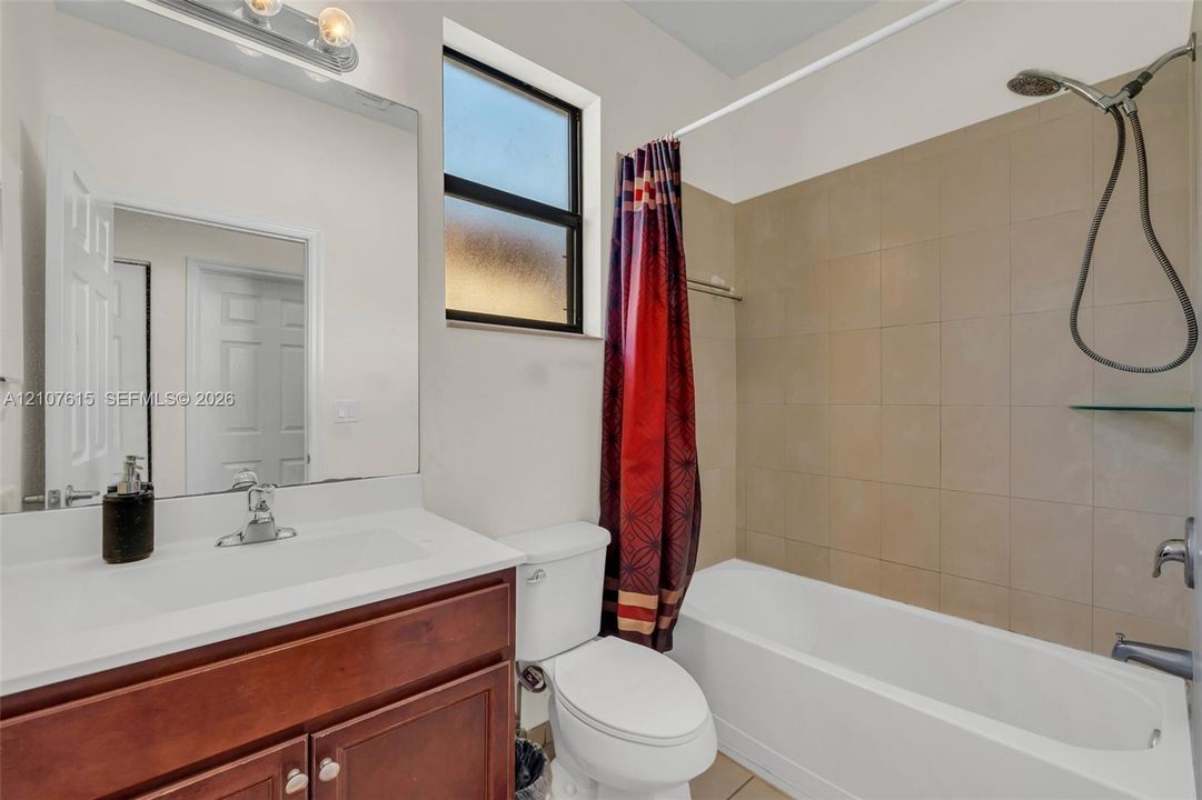 Bathroom featuring a wood-finish vanity with a rectangular sink, large wall-mounted mirror, overhead vanity light, and a tiled tub-shower combination with a handheld shower fixture