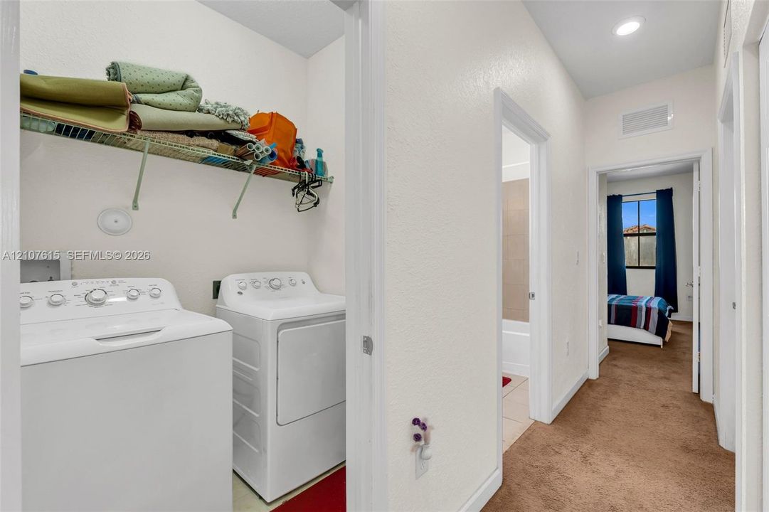 Laundry room featuring a wire shelving unit and recessed ceiling lighting, leading to a space with tan carpeting