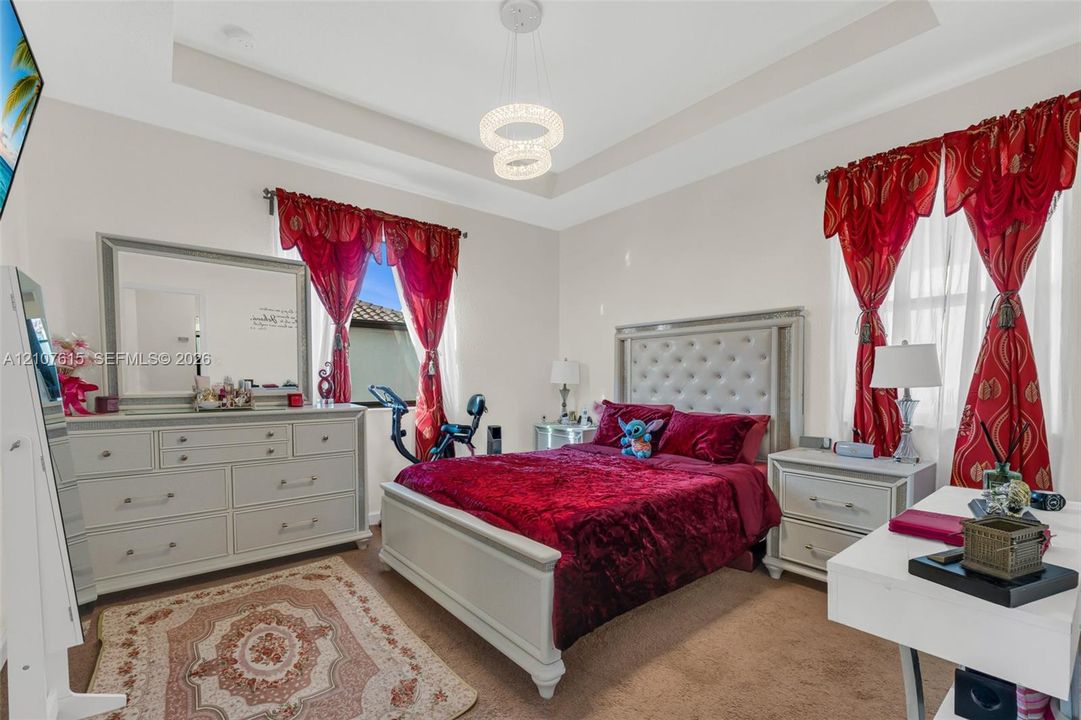 Bedroom featuring a tray ceiling, modern tiered light fixture, neutral wall palette, and wall-to-wall carpeting