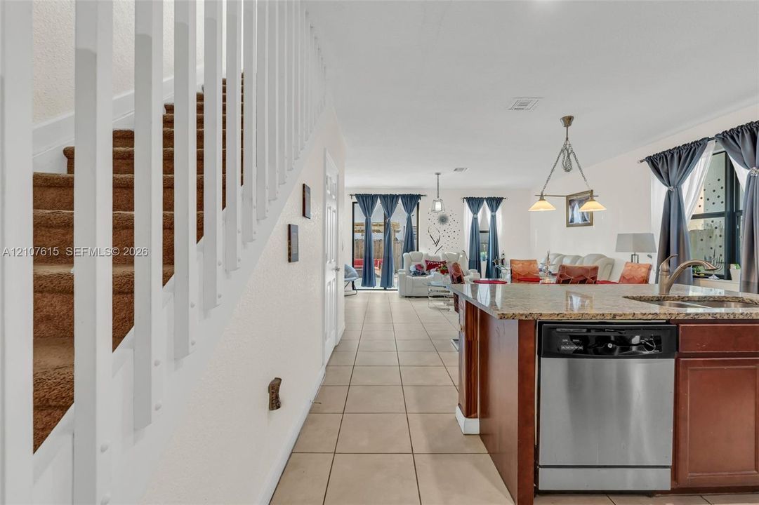 Kitchen island featuring stone countertops and stainless-steel dishwasher, ceramic tile flooring, and staircase with white railings