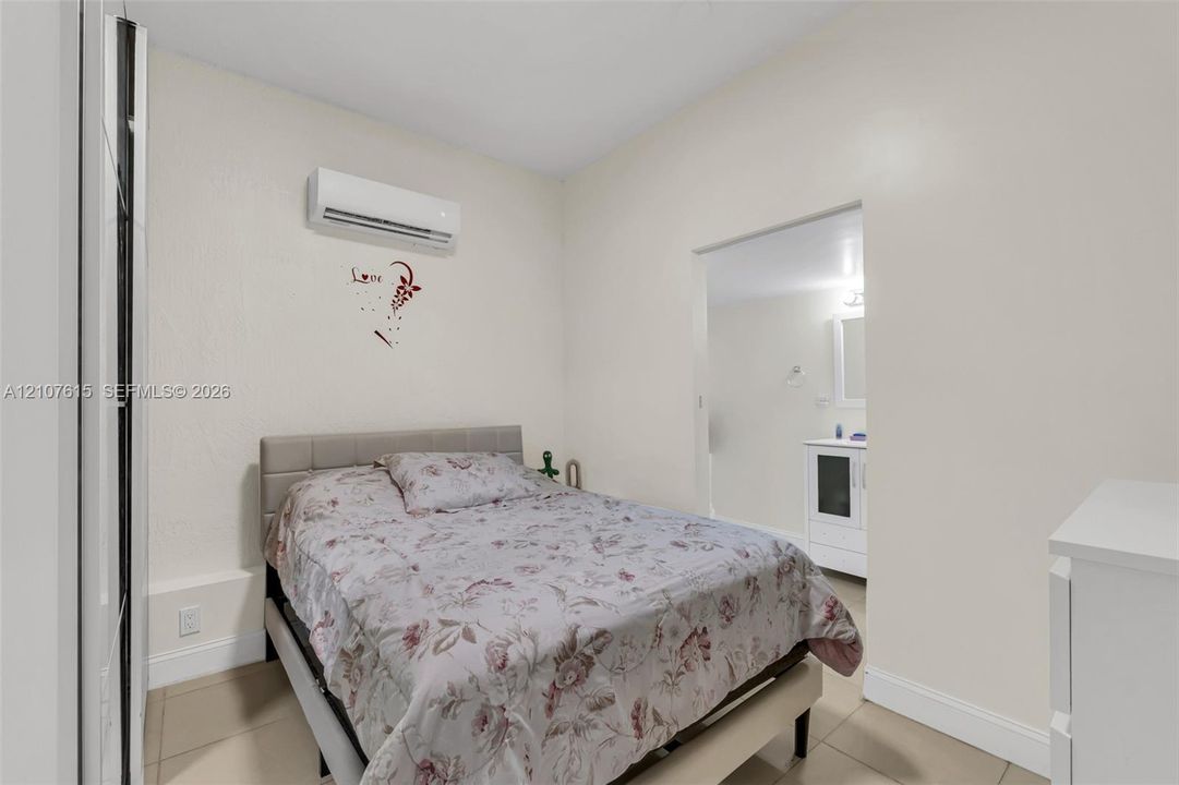 Wall-mounted ductless air conditioning unit, neutral tone wall-to-wall tiling, and white cabinetry featuring a rectangular sink with integrated storage
