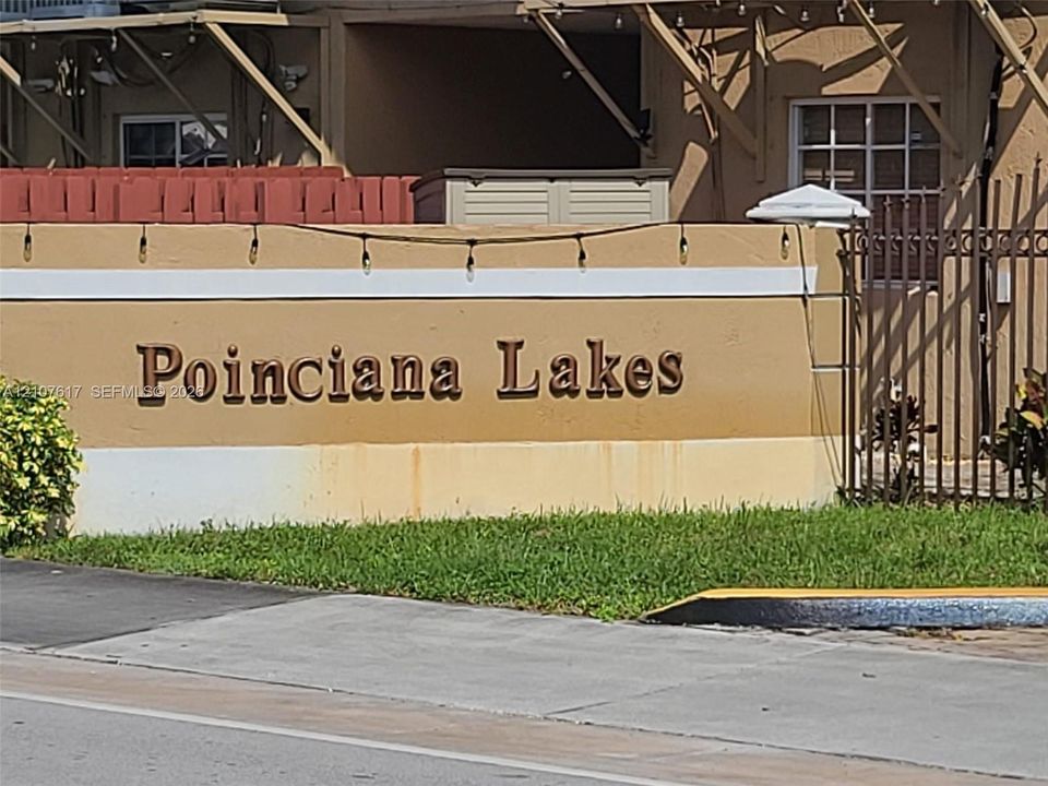 Stucco monument signage featuring dimensional lettering, landscaped greenery, and iron fencing