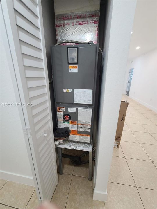 Utility closet featuring a central HVAC air handler unit enclosed by louvered bi-fold doors