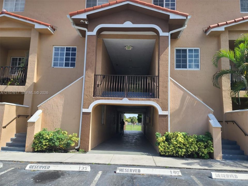Stucco exterior with an arched entryway, elevated balcony featuring metal railings, and two sets of concrete exterior stairs