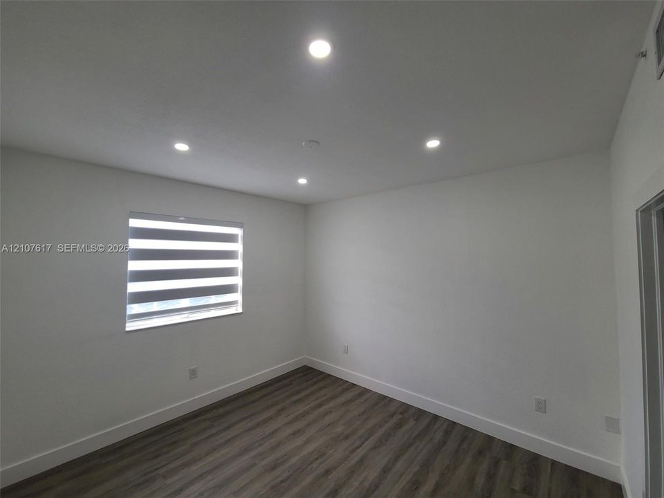 Neutral-toned room featuring wood-finish flooring, recessed lighting, and a window with adjustable roller shades