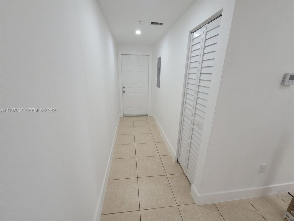 Interior hallway featuring neutral ceramic tile flooring, a six-panel door, and closet doors with louvered panels