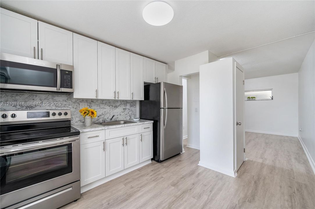 Kitchen featuring white shaker-style cabinetry, stone-finish countertops, full-height decorative backsplash, stainless steel appliances, and wood-finish flooring