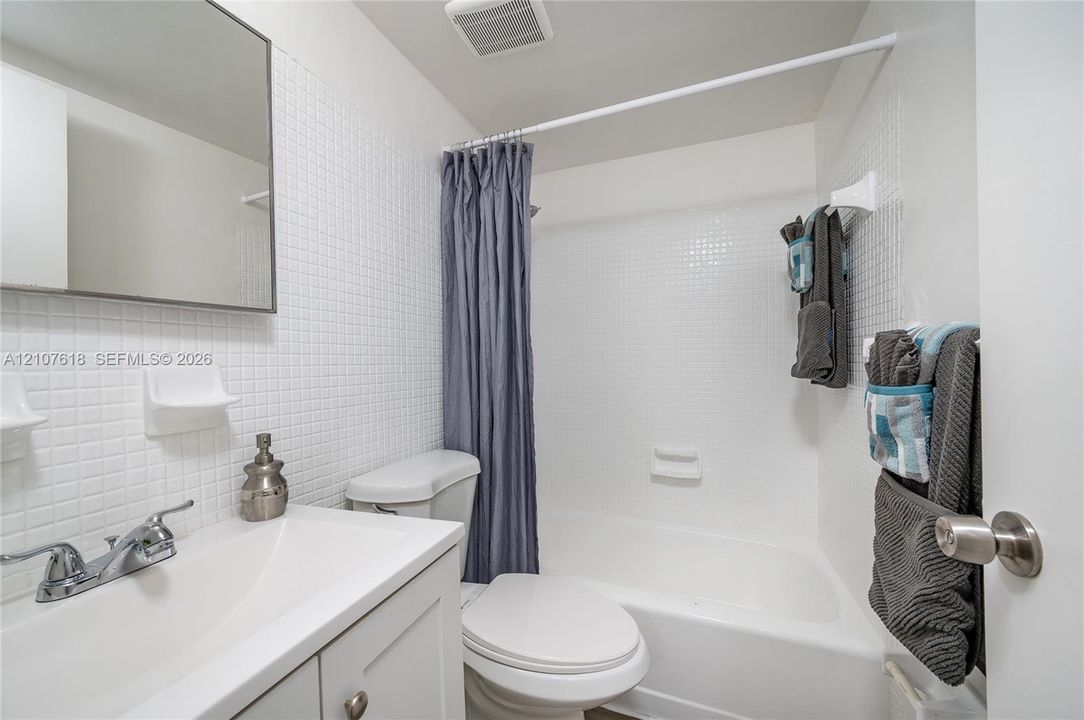 Bathroom featuring a white vanity cabinet, rectangular undermount sink, chrome faucet, tiled wall surfacing, and a built-in shower and tub combination
