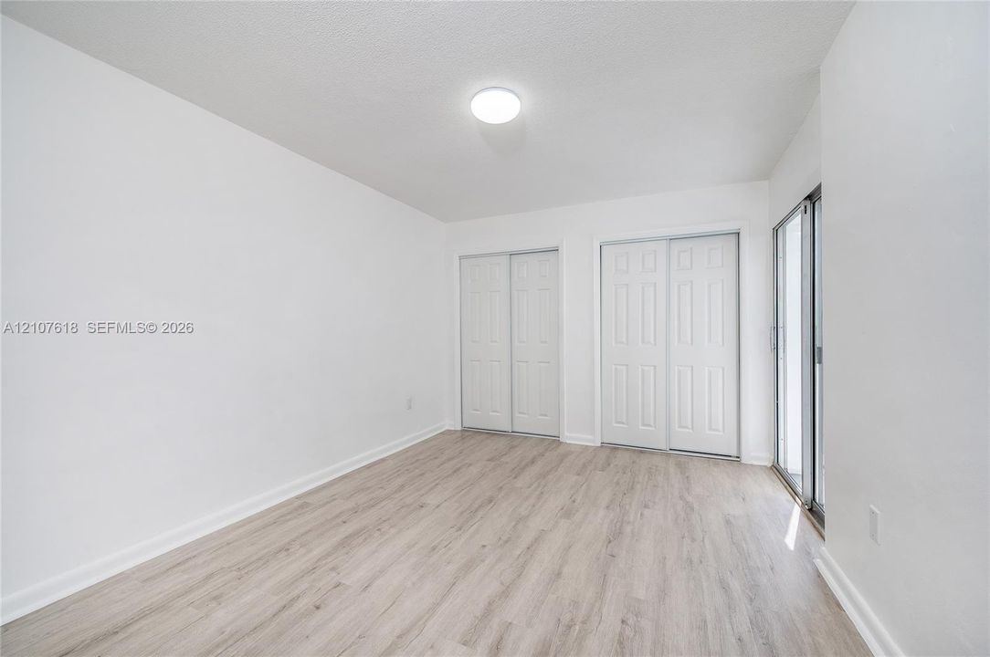 Neutral-toned wood-finish flooring, two sets of white paneled closet doors, and a sliding glass door